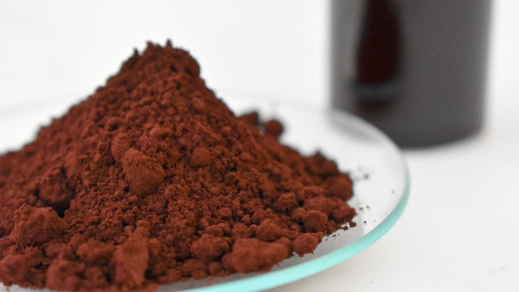 brown oil dye powder on watch glass with glass beaker in background